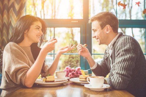 Couple on a date in a sunny cafe eating cake
