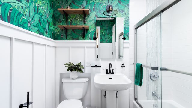 A bright white bathroom with a beautiful, colorful green leaf wallpaper.
