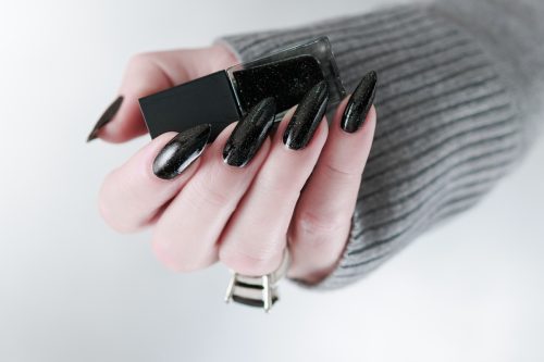Female hands with long nails and black manicure holding a bottle of nail polish