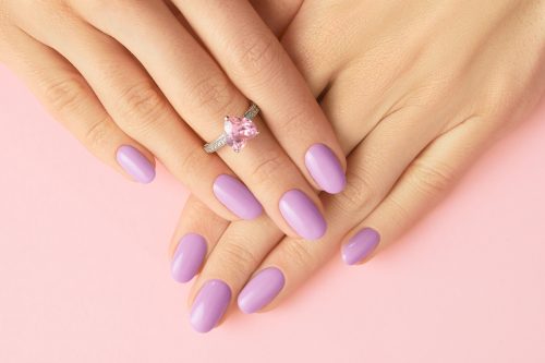 Woman's hands with lavender nail polish wearing a pink gemstone rink on a pink background