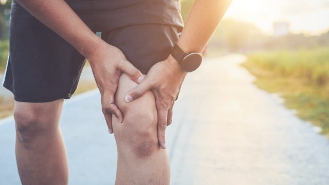 man use hands hold on his knee while running on road in the park.