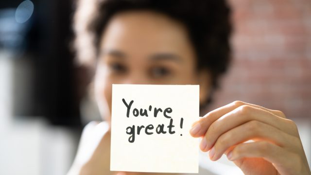 woman holding up a post-it note saying "you're great"
