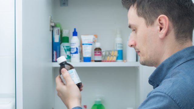 A man looking at a bottle he has just taken from his medicine cabinet