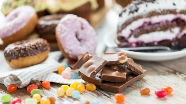 junk food, sweets and unhealthy eating concept - close up of chocolate pieces, jelly beans, glazed donuts and cake on wooden table