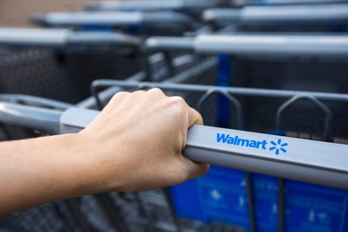 Woman taking shopping cart near supermarket Walmart. Closeup on female hand holding shop trolley with sign of the shop
