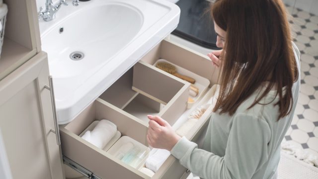 Top view of a woman organizing the drawer underneath the sink in her bathroom