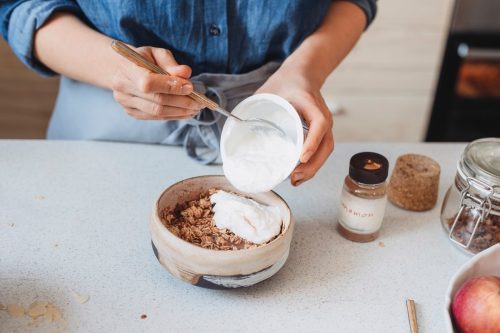 Making breakfast: unrecognizable woman adding yoghurt to oatmeal.