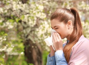 Sneezing young girl with nose wiper among blooming trees in park
