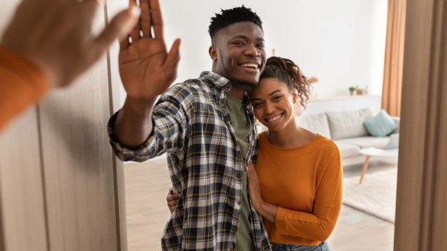 happy couple standing in opened doors of their house waving goodbye to guests