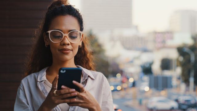 Shot of a young businesswoman texting while standing outside on the office balcony