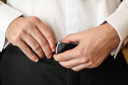 Mid adult unrecognizable man in shirt and trousers fixing his belt buckle