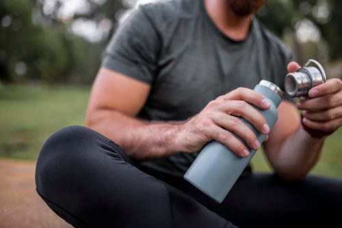 Close up of a reusable water bottle in a human hand, concept of thirst, rehydration and decreasing single use plastic