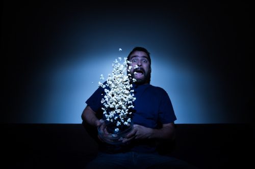 Scared man watching a horror movie and jumping with popcorn flying allover