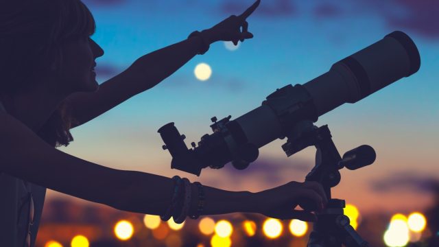 woman with a telescope pointing at the night sky