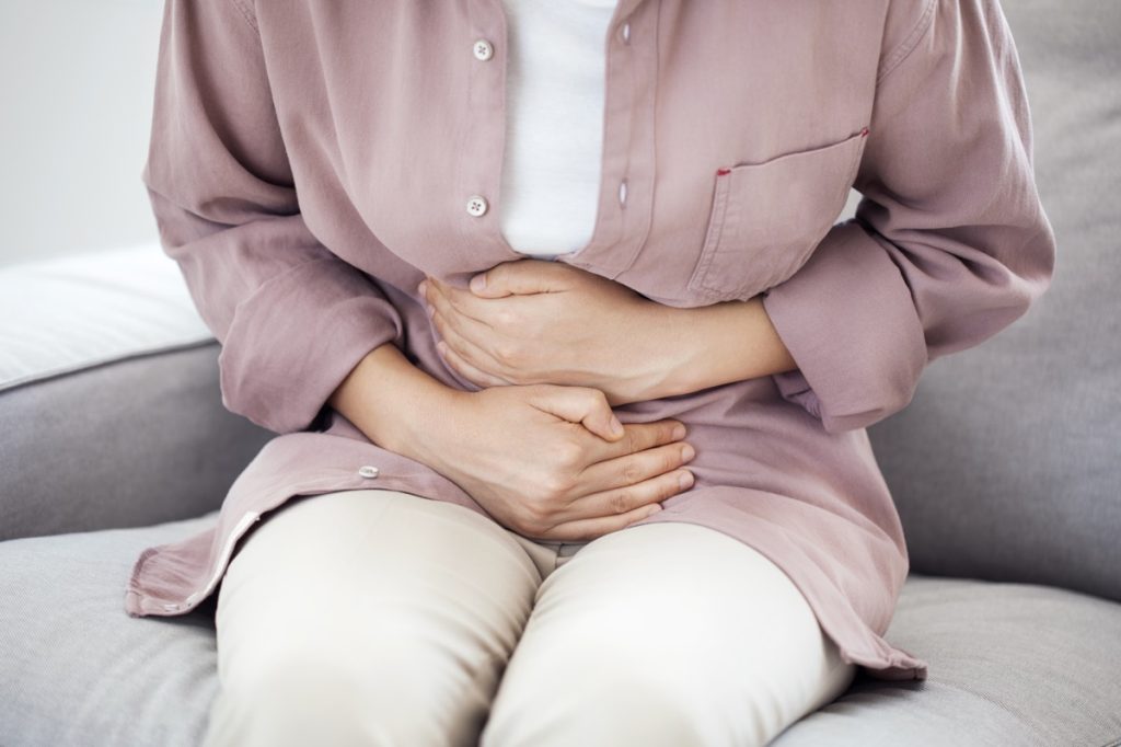 woman sitting on couch and clutching her stomach