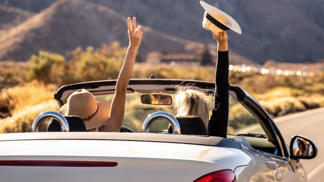 Two women driving on a highway while on a road trip.