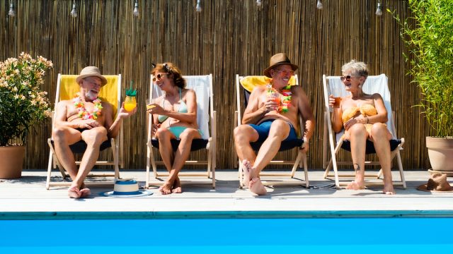 Group of cheerful seniors sitting by swimming pool outdoors in backyard.