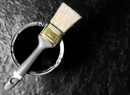 Open can of black paint and a paint brush against a black background