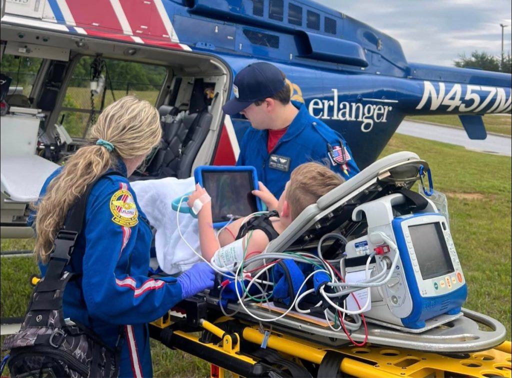 A young boy on a stretcher being placed onto a medical helicopter by two EMS workers