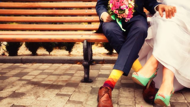 Chest-down view of a bride and groom on a bench wearing colorful shoes and socks