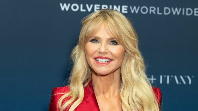 Christie Brinkley wearing a red satin blazer against a blue background