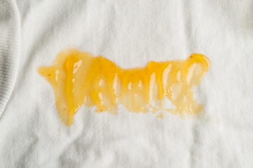 Close up of a white shirt with a large stain of yellow jam on it