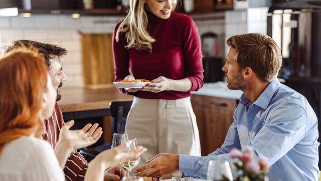 Woman is serving her friends at the dining room table during a dinner party.