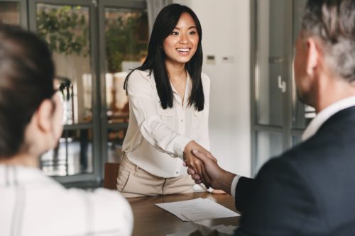 woman standing across table from woman and man, she's shaking the man's hand