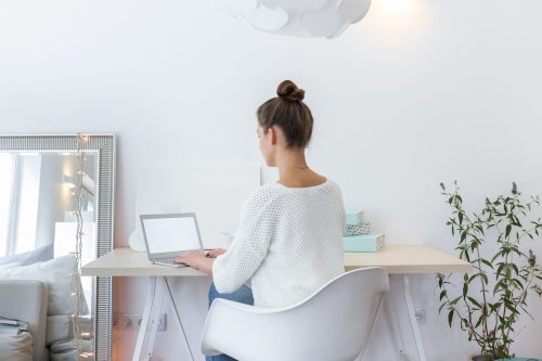 Rear view of a young girl working on her laptop at her desk in an all-white home office