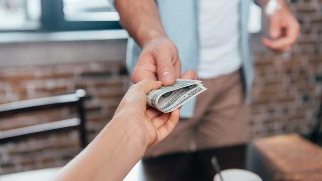 Close up of someone handing a person dollar bills