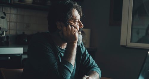 older man sitting at home in the dark looking thoughtful