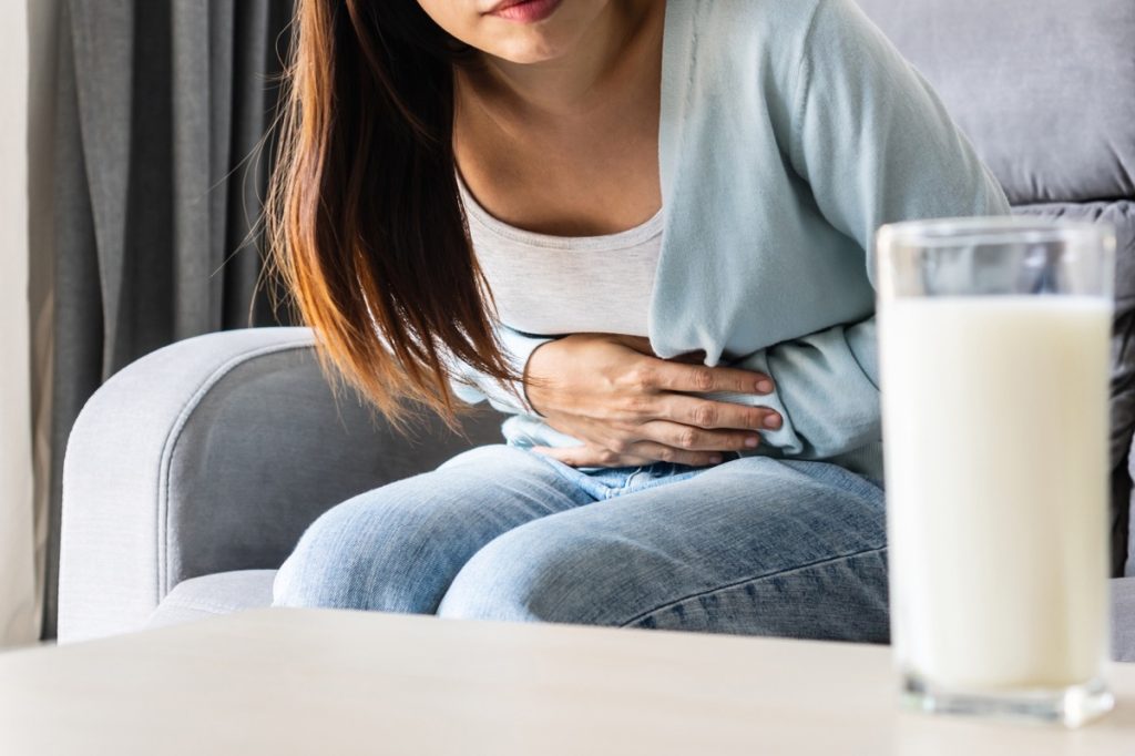 Unhappy young woman having bad stomach ache with glass of milk on table.