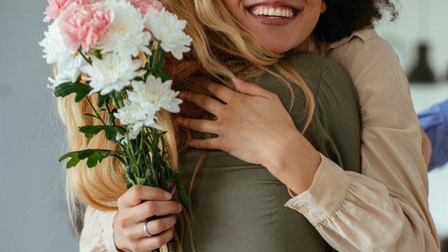 Portrait of two women hugging each other and holding flowers.