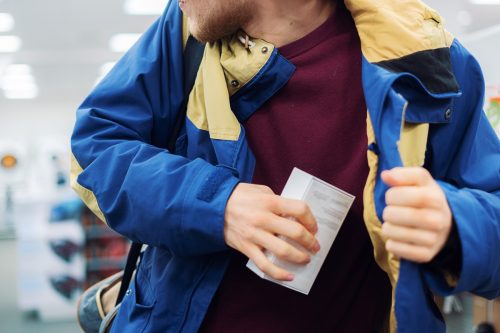close up consumer thief’s hands putting the new gadget in the pocket in the store