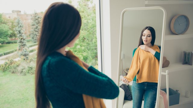 Young woman trying on yellow sweater in mirror