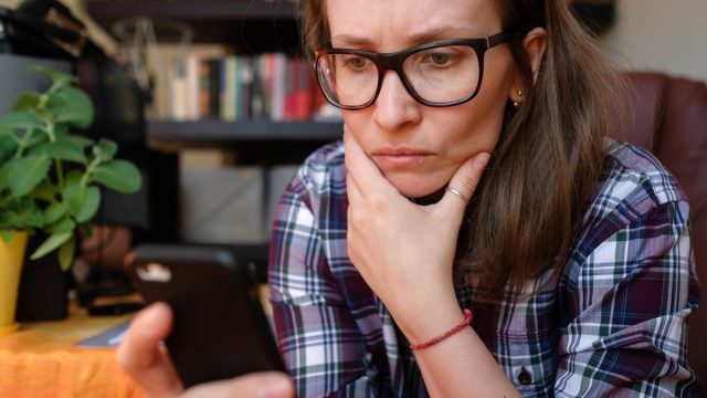 A woman reads news from a mobile phone and looks freaked out and anxious.