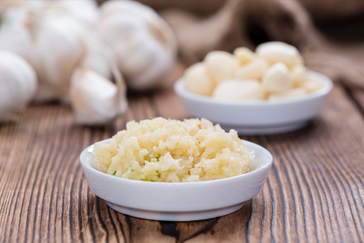 Crushed Garlic on wood surface with whole garlic in the background