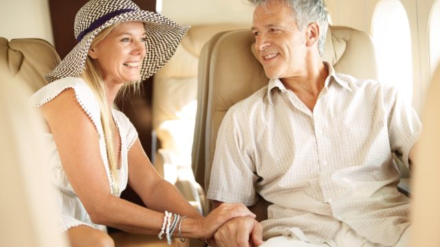 Ready for a romantic holiday. Smiling senior couple holding hands on an airplane heading overseas.
