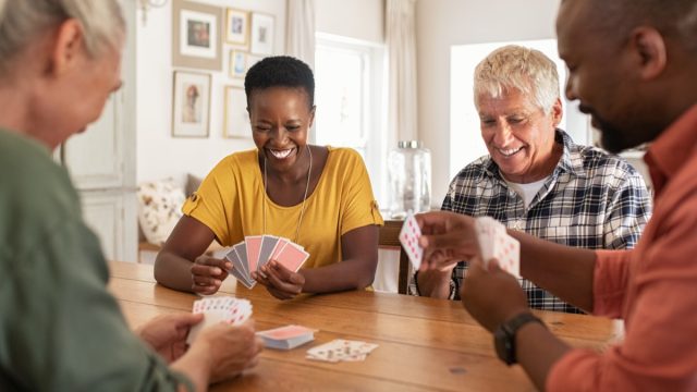 Retired multiethnic people playing cards together at home. Happy senior friends with african couple playing cards. Cheerful active seniors playing game at lunch table.
