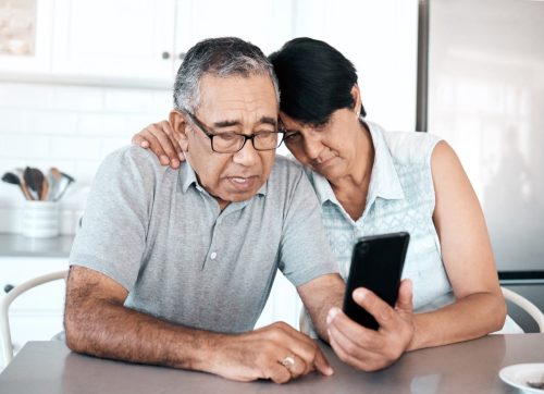 Shot of a senior couple looking unhappy while using a phone at their kitchen table