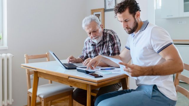 Son Giving Senior Parent Financial Advice at Home. Adult Son Doing Accounts Together With His Senior Father at Home, Planning New Purchase. Family Budget and Finances.