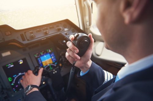 Close up pilot hand taking by portable radio set in cabin while navigating plane. Occupation and communication concept
