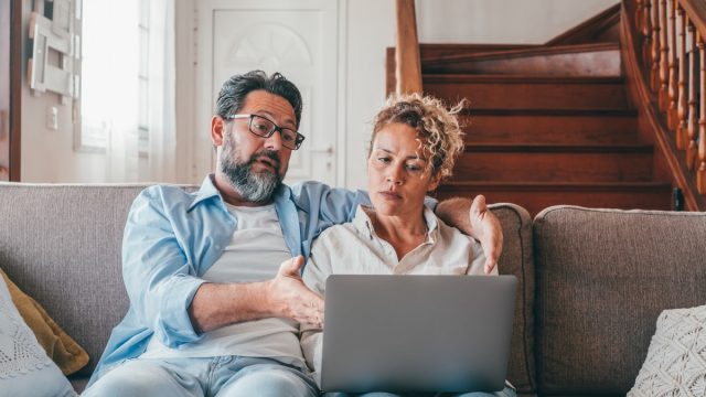 Shocked couple looking at laptop screen frustrated by unexpected bad news online. Husband and wife disappointed and feeling anxious on losing money in online lottery,