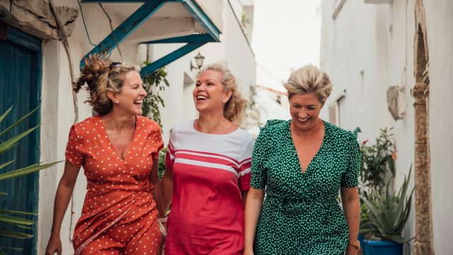 Three happy female friends walking through a European town on vacation, wearing colorful sundresses
