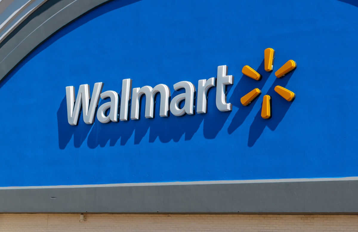 Horizontal, medium closeup of "Walmart" superstore's exterior facade brand and logo signage in white letters against a reflective, blue background and yellow logo