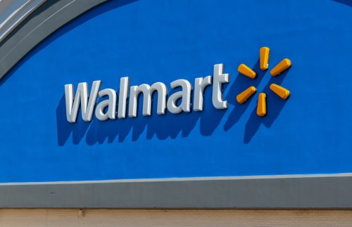 Horizontal, medium closeup of "Walmart" superstore's exterior facade brand and logo signage in white letters against a reflective, blue background and yellow logo