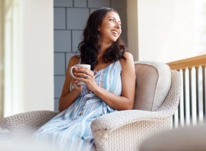 A woman drinking a cup of coffee or tea while sitting on her front porch