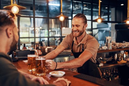 Charming young bartender in apron serving beer and smiling