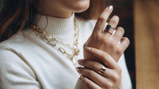 closeup of a woman in a cream turtleneck sweater wearing a gold necklace and two gold rings