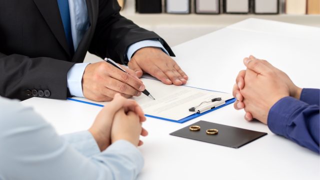 Close up of a couple signing divorce papers with attorney and their rings on the table